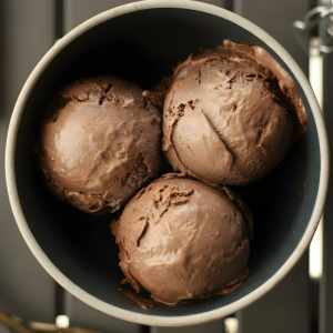 Three scoops of classic chocolate ice cream in a dark bowl, with a smooth, slightly softened texture.