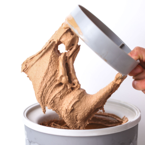 Chocolate-only ice cream made with xanthan gum being lifted from a tub with a spatula, stretching to show its creamy texture.