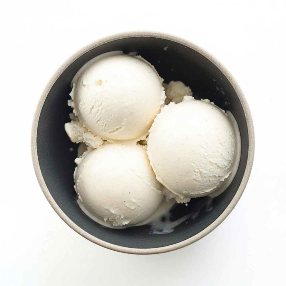 Three scoops of white chocolate ice cream made with cornstarch in a ceramic bowl, photographed from above on a white background.