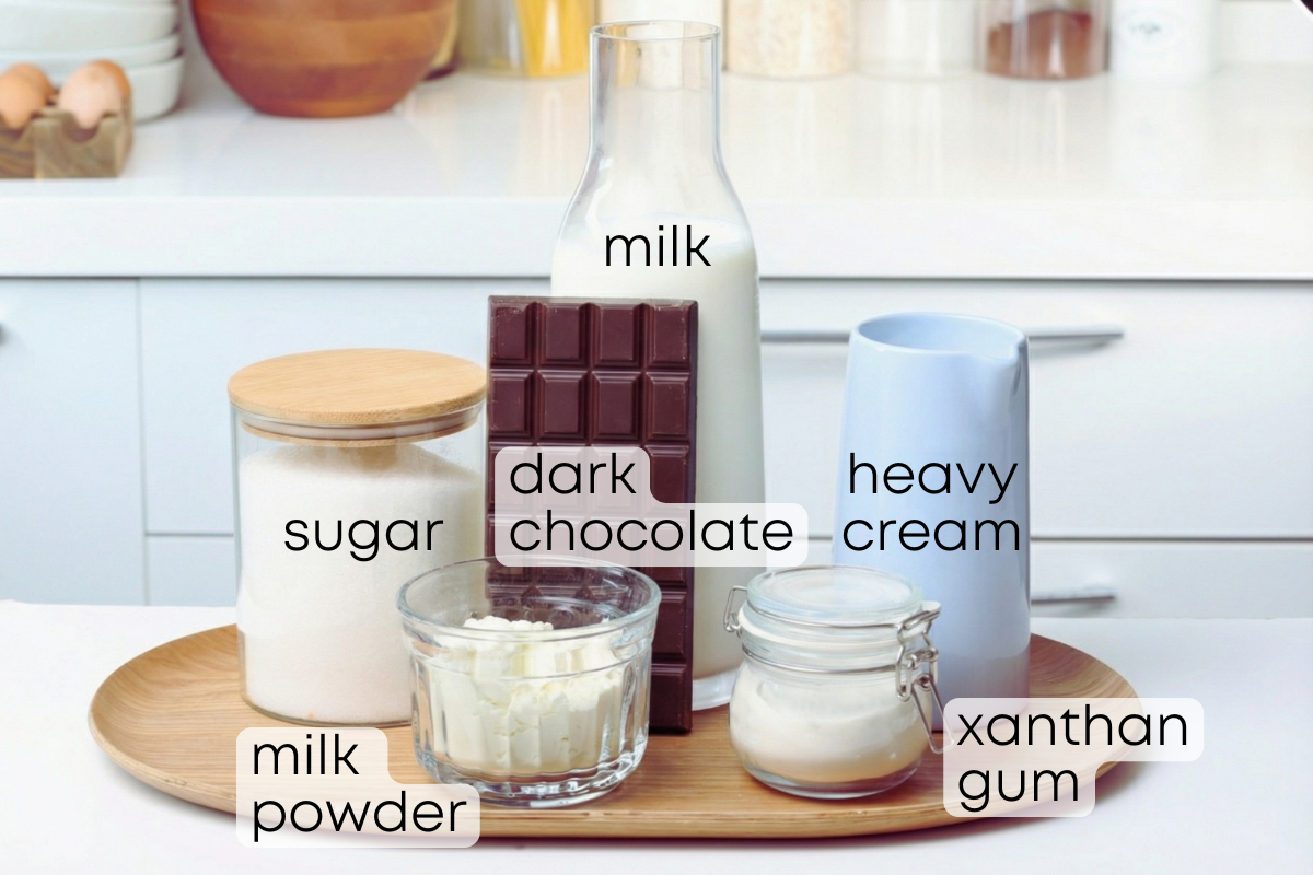 Ingredients for milk chocolate ice cream: milk, heavy cream, sugar, dark chocolate, milk powder and xanthan gum arranged on a wooden board in a bright kitchen.